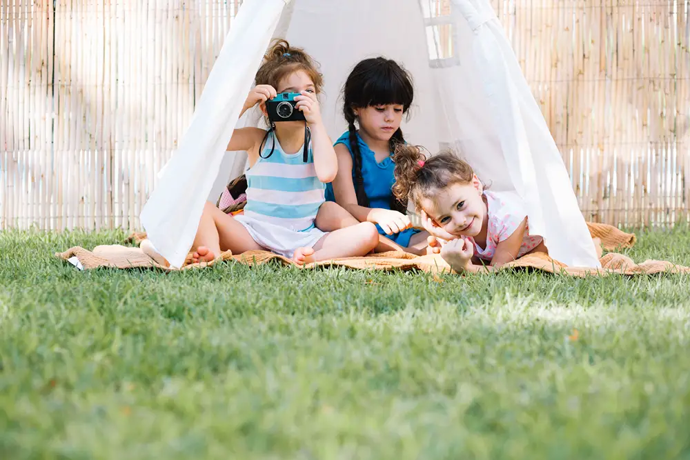 Three girls playing in tent on backyard lawn.
