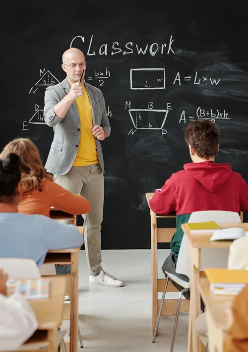 A male teacher stands in front of blackboard teaching a class.