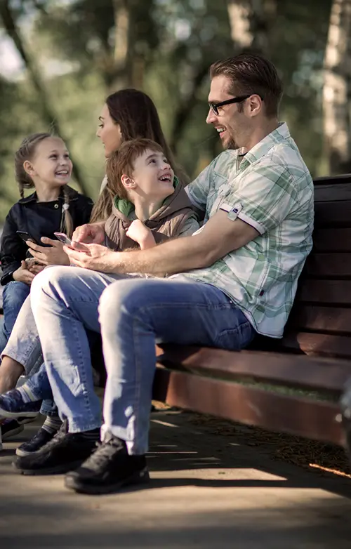 Parents of a girl and a boy talk with their kids on a park bench.