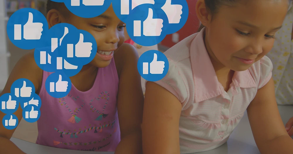 Two girls smiling as looking down at tablet as like emojis icons pop up around them.