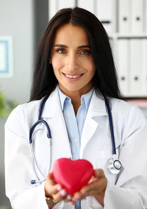 A female health professions smiles as she holds a plastic toy red heart.