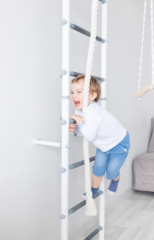 A happy toddler climbing up a ladder on an indoor climbing gym.