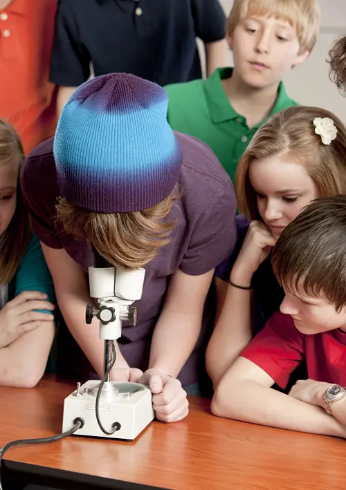 Group of middle school children gathered around a table looking through a microscope during a hands-on science lesson.