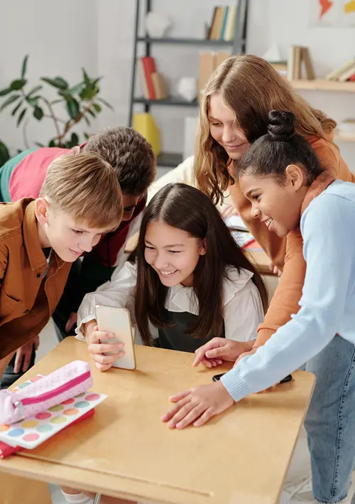 Middle school aged students gather around a girls desk as they all look at her smartphone.