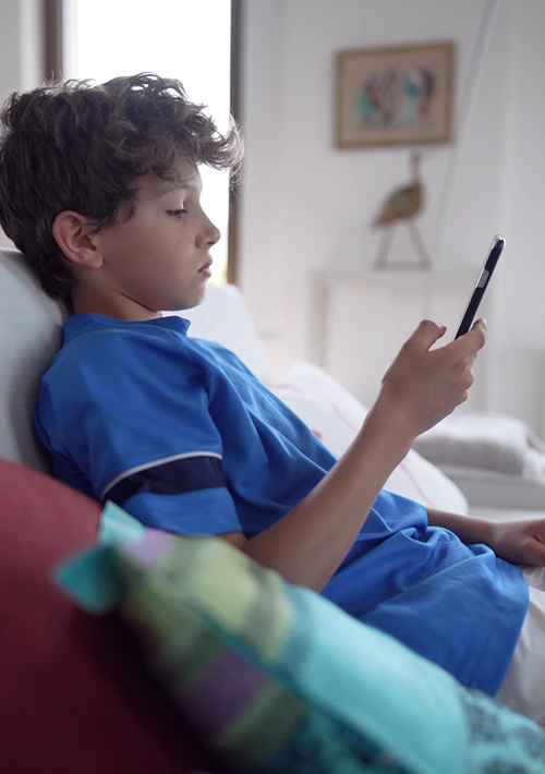 A teen boy lays in his bed while scrolling on his smartphone.