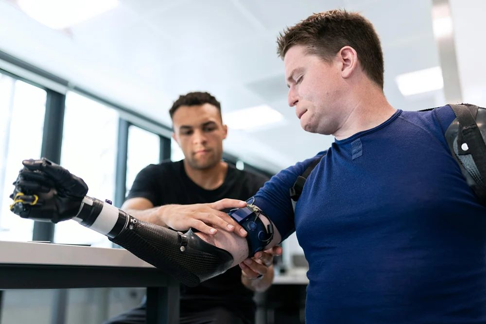 A specialist fitting a high-tech prosthetic arm on a man, showcasing the application of assistive technology in a clinical setting.