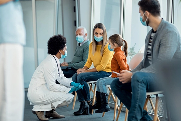 Female African American doctor bends down to talk to child and her family in a waiting room.