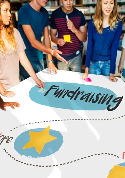 A group of students standing around a work table creating a fundraising sign.