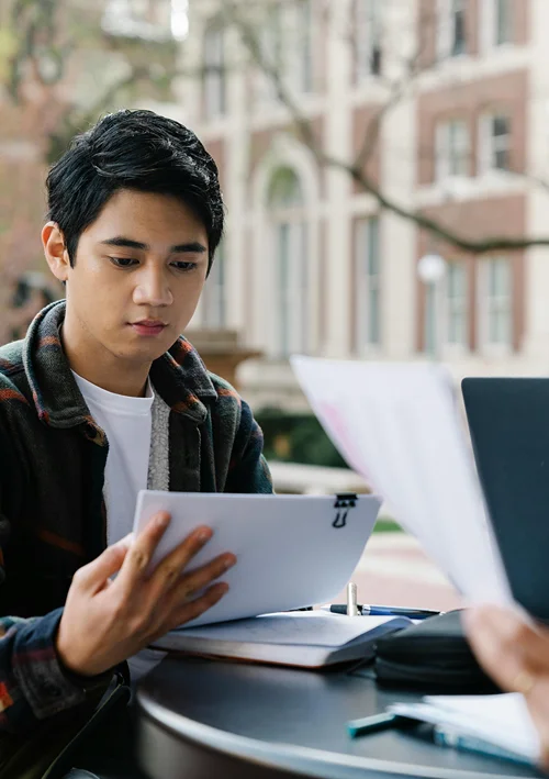 A male Asian student studies outside in front of university.
