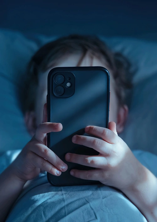 A child's face is blocked by his smartphone has he lays in bed at night.