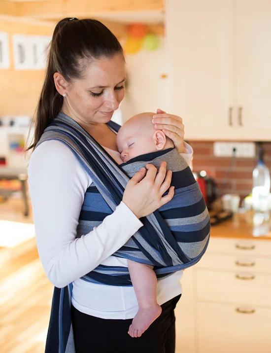 Mom with baby in a baby carrier stands in a kitchen