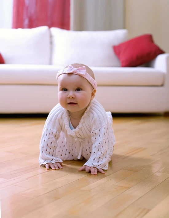 Happy baby crawling on hardwood floor in living room.