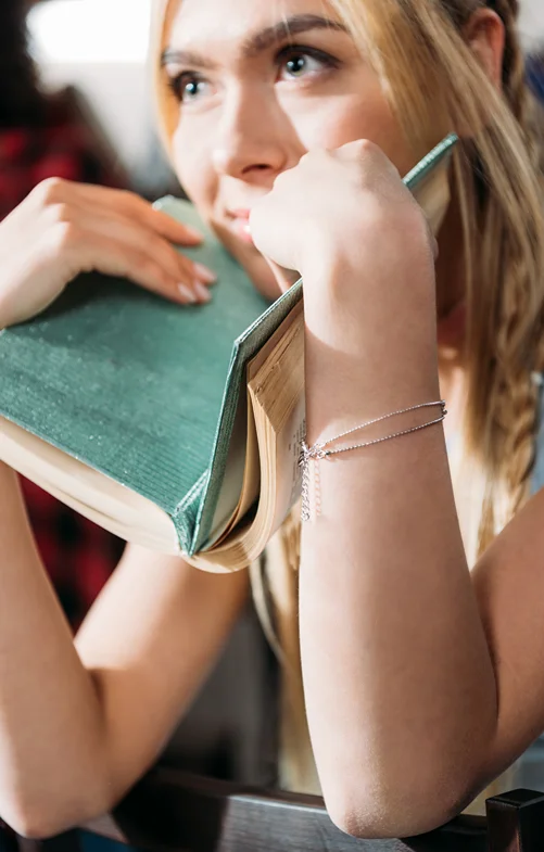 loseup of a teen girl looking off into the distance over the book she is holding.