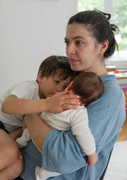 A fatigued looking mother holding a baby and her 5 year old son.