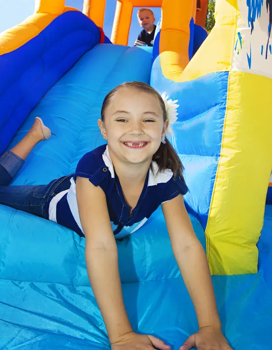 A smiling girl missing her two front teeth is having a blast in a bouncy house.