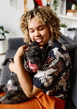 A happy black girl hugs a black dog as he sticks out his big red tongue.