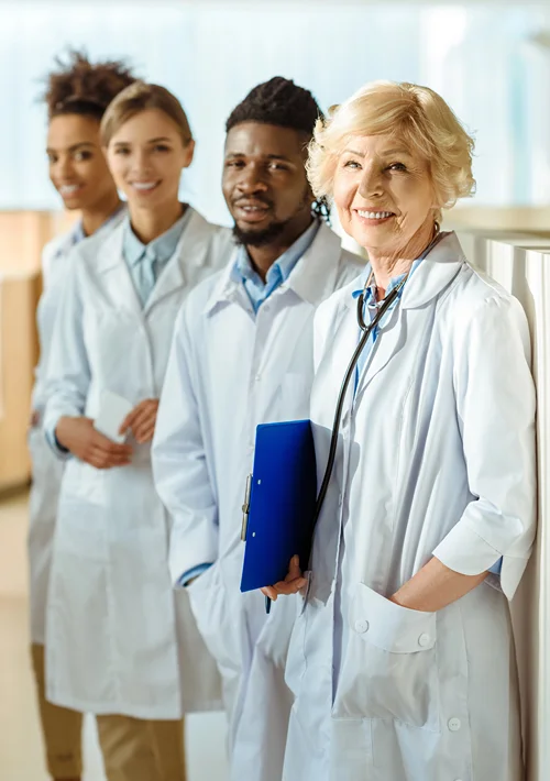A diverse group of smiling Doctors of Nursing Practice (DNP) wearing white lab coats and stethoscopes in a modern hospital hallway.