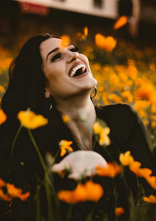 A middle aged woman looks to the sky with joyful look as she stands in a field of flowers.