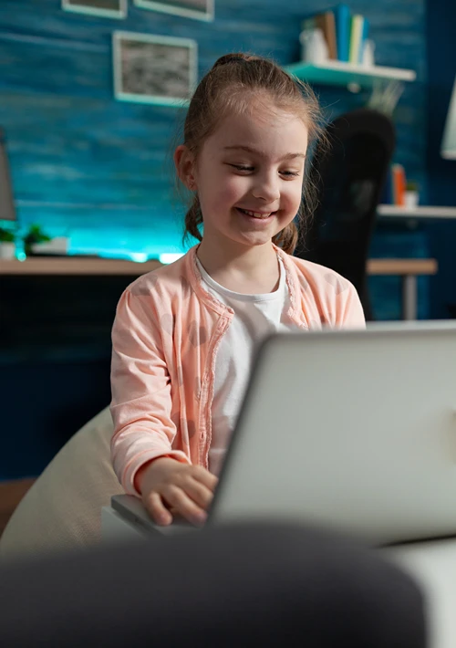 A little autistic girl smiles as she browses on a laptop.