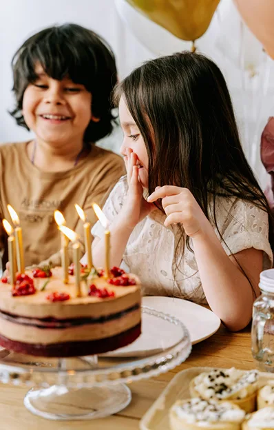 A girl talks to a boy seating beside her as candles burn on her birthday cake.