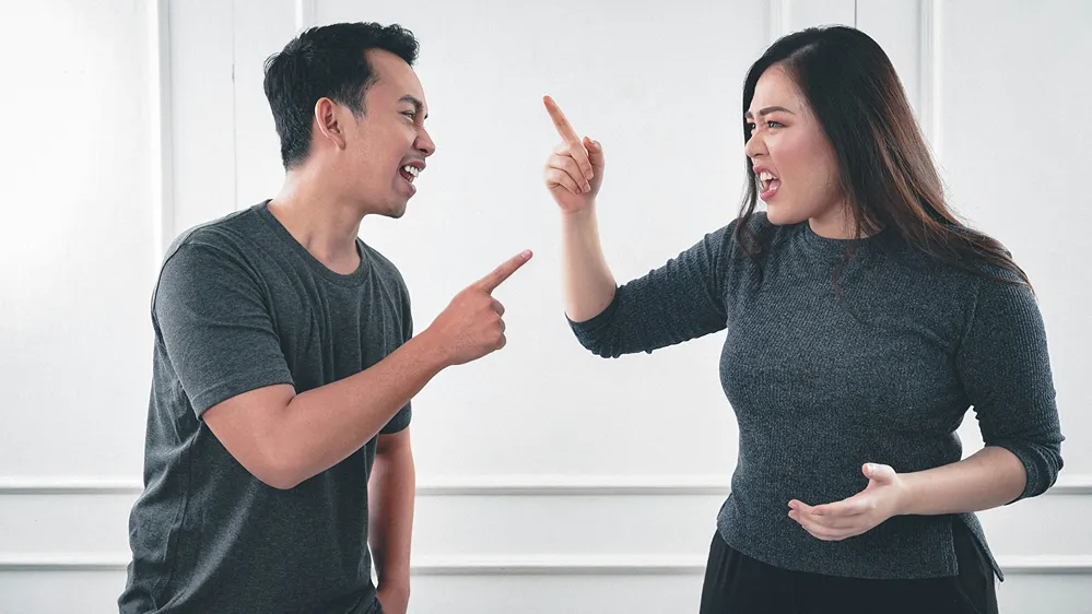 A man and woman point fingers at each other in a robust argument.