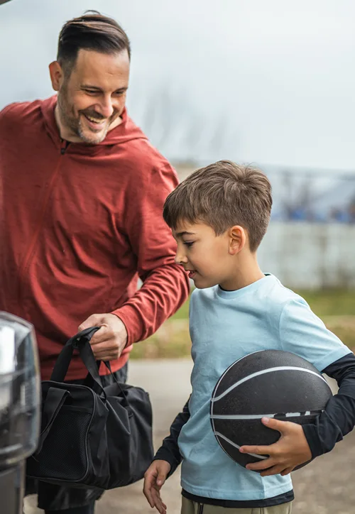 Boy holds a soccer ball while dad holds duffle bag as they get into a vehicle.