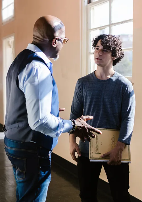 School counselor and teen boy speak in a school hallway.