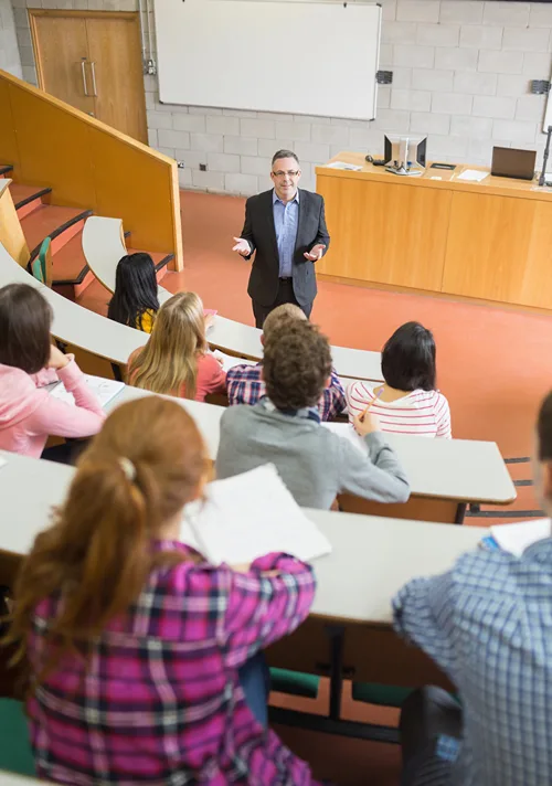 View from top of a lecture hall filled with young students looking down at a male teacher.