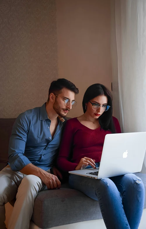 A woman working on a laptop at home as her male partner looks over her shoulder.