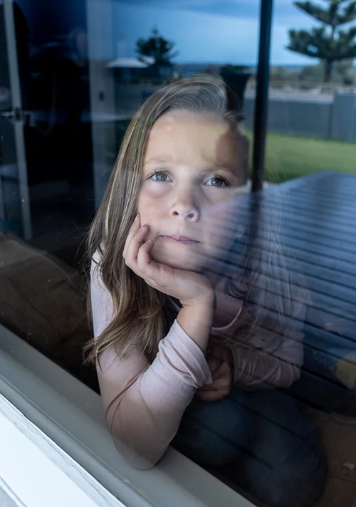 Bored young girl resting chin on hands while looking out window on a summer day.