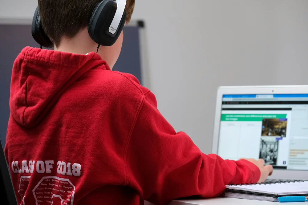 View from behind a boy with headphones engaged in virtual school on his laptop.