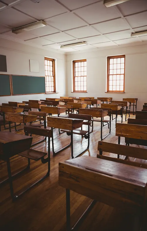 Sunlight shines in through the windows of a classroom of empty desks.