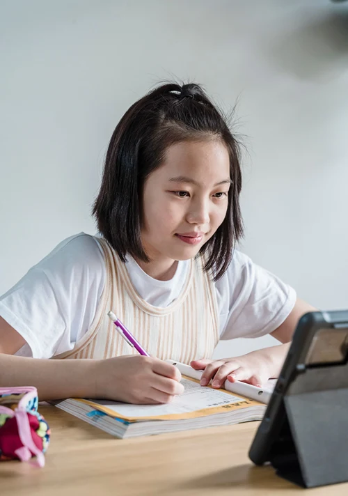 Girl taking notes during virtual school on a tablet at home.