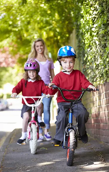 Boy and girl with helmets ride their bikes slowly as mom walks behind.