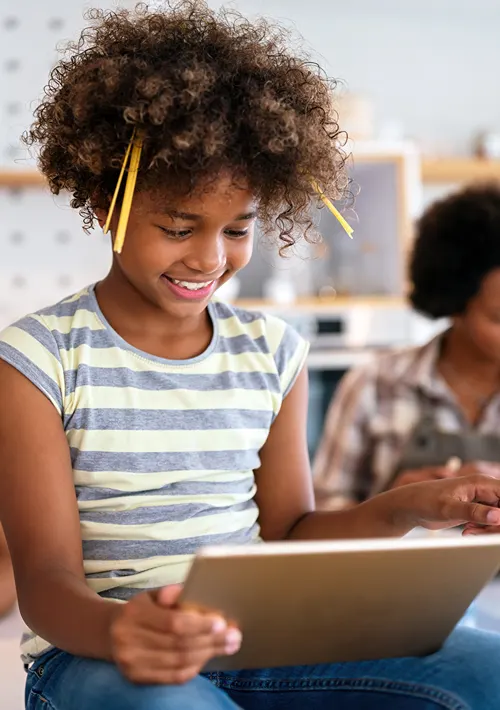 Smiling middle school ages African American girl playing a game on a tablet in class.