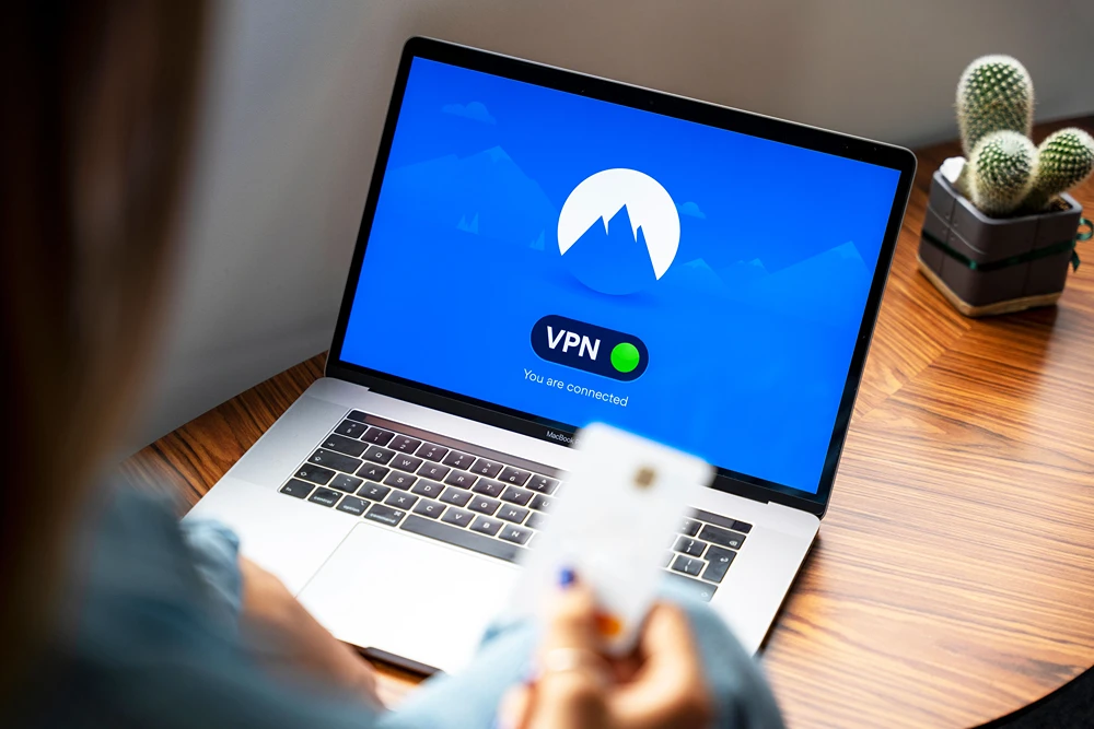 A person holds up a credit card while VPN webpage is shown on a laptop screen.