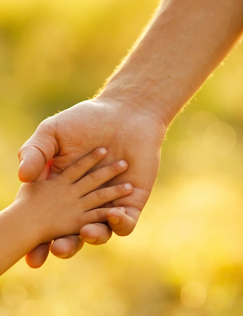 An adult hand reaches down to take the hand of a small child.