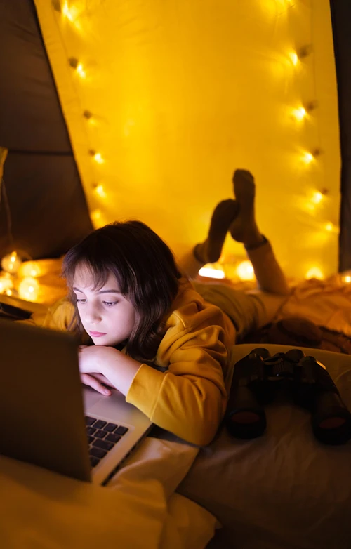 11 year old girl playing a game on a laptop in her bedroom at night.