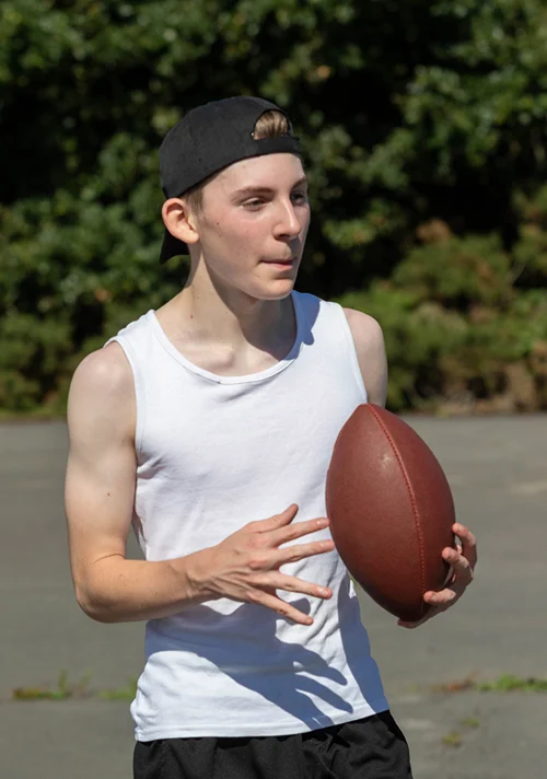 A male teen in a muscle shirt is getting ready to throw a football in a park.