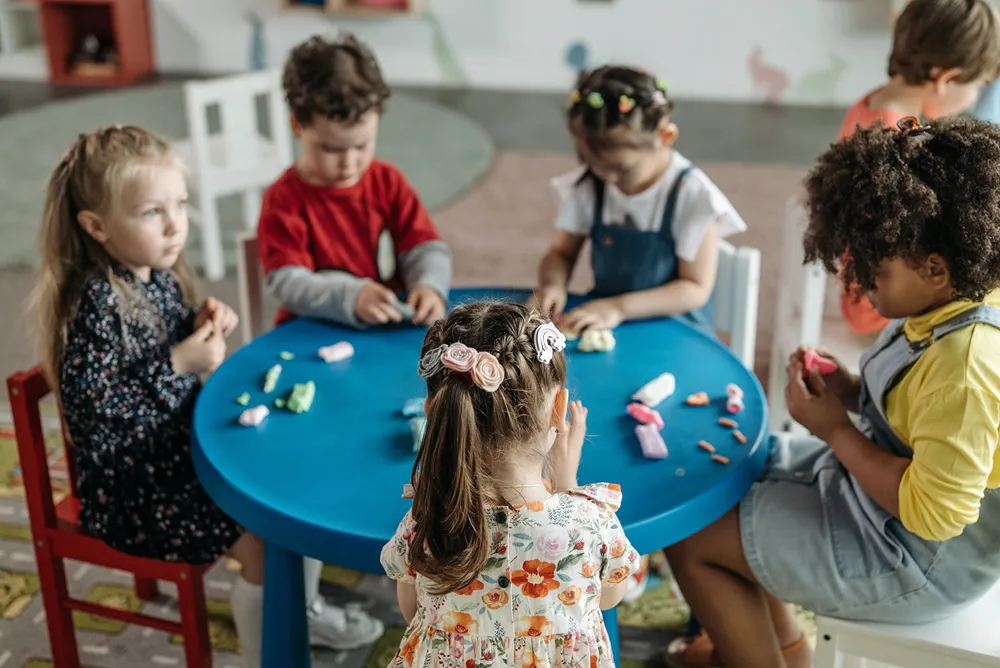 Kids in preschool seated at a round table playing with clay dough.