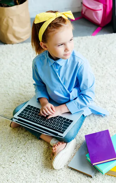 A young girl sits on living room floor with laptop and looks off to the side.