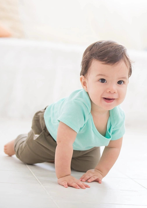 A baby boy eagerly crawls on the carpet towards something or someone.