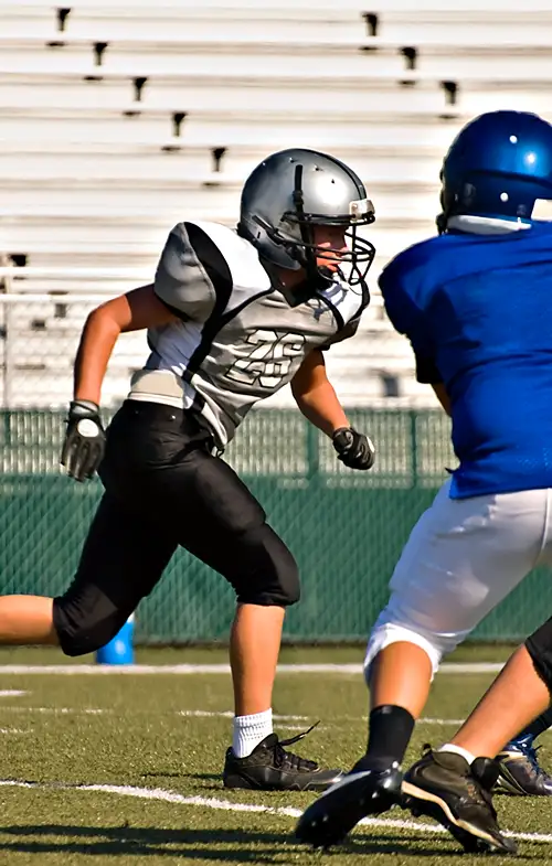 A boy runs down a football field towards a group of other players.