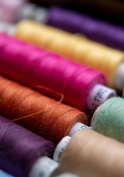 Close-up of brightly colored sewing thread spools arranged diagonally, featuring vibrant pink, orange, and purple threads.