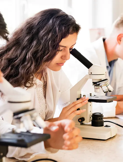 Well dressed female student looking through microscope in a lab.