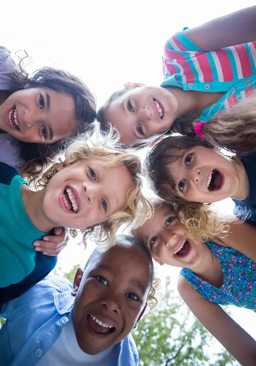 Mix of boys and girls outdoors smiling for a group photo.
