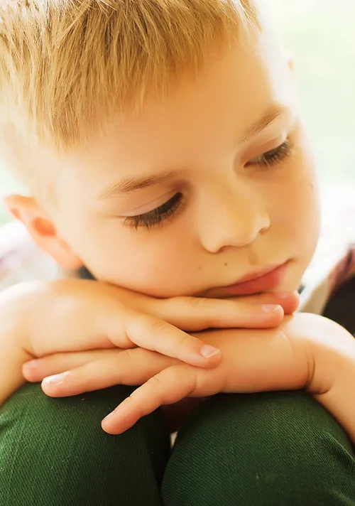 A little boy looks away has he sits with is hands and head resting on his knees.