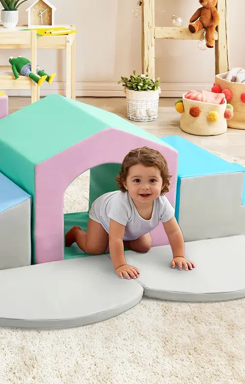 A smiling toddler crawling out of a brightly colored, soft foam playhouse structure.