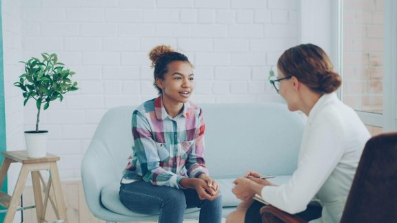 A teen girl smiles while speaking with her therapist.