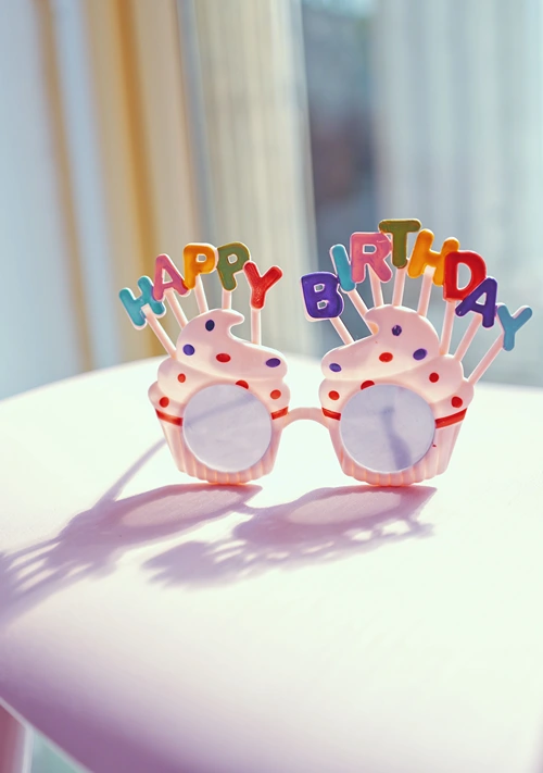 Novelty happy birthday sunglasses with pink cupcake frames and colorful letters.